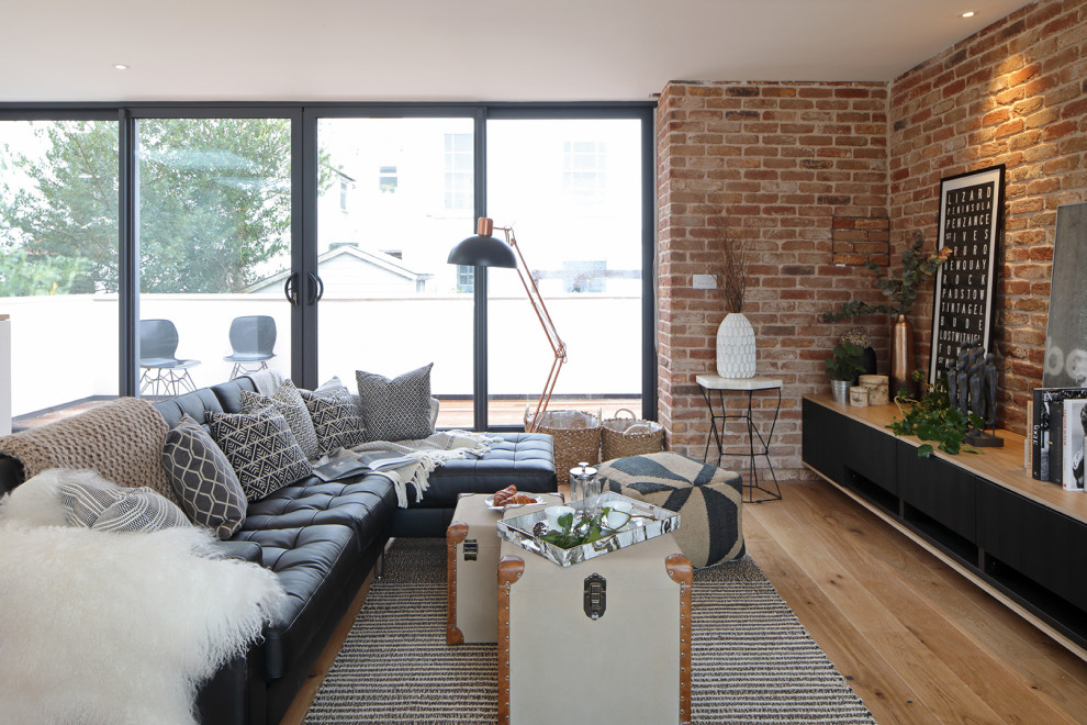 Modern open plan living room feature wall in Other with white walls, light hardwood flooring and brick walls.