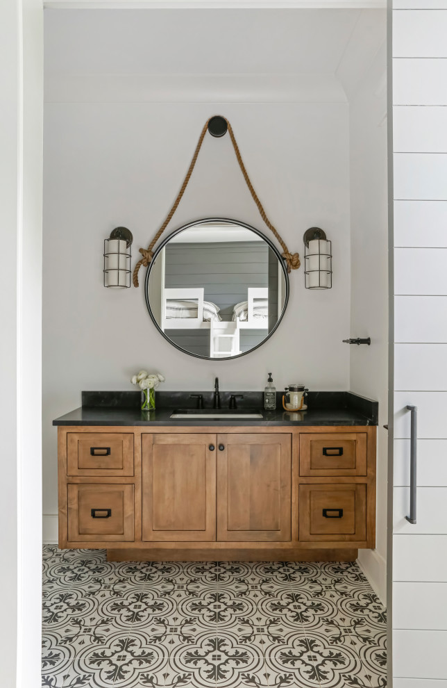 Photo of a large country kids bathroom in Nashville with shaker cabinets, medium wood cabinets, a shower/bathtub combo, white tile, subway tile, white walls, porcelain floors, an undermount sink, marble benchtops, white floor, a shower curtain, black benchtops, a single vanity and a built-in vanity.