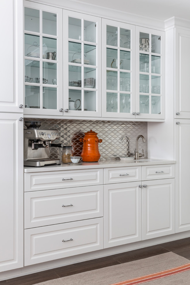 Large transitional l-shaped dark wood floor kitchen photo in New York with an undermount sink, raised-panel cabinets, white cabinets, solid surface countertops, metallic backsplash, metal backsplash, stainless steel appliances and an island