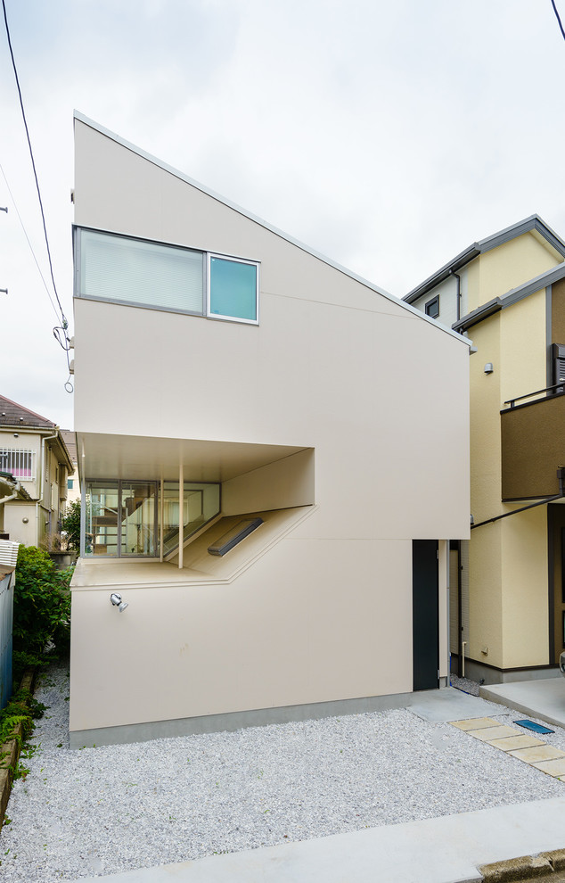 This is an example of a contemporary beige house exterior in Tokyo with a shed roof.