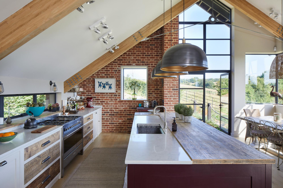 This is an example of a farmhouse galley open plan kitchen in London with a submerged sink, shaker cabinets, white cabinets, stainless steel appliances, medium hardwood flooring, an island, brown floors, white worktops, exposed beams and a vaulted ceiling.