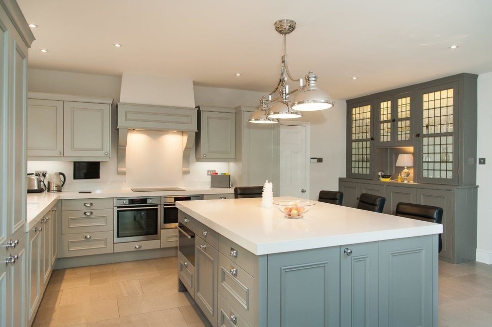 Photo of a large contemporary u-shaped eat-in kitchen in Hertfordshire with a drop-in sink, shaker cabinets, green cabinets, granite benchtops, white splashback, limestone splashback, stainless steel appliances, slate floors, with island and beige floor.