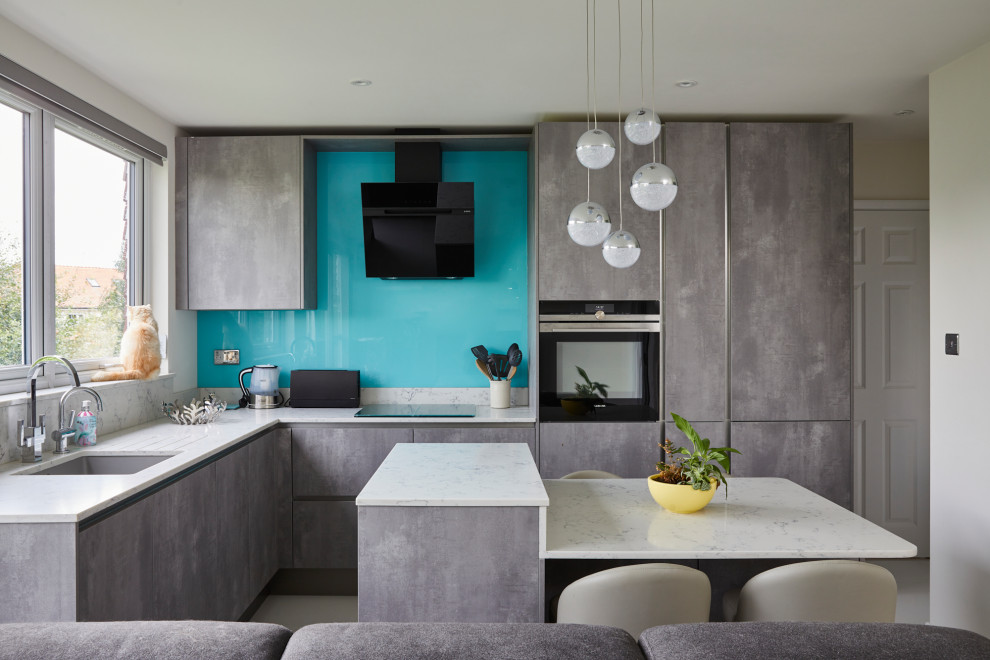 Photo of a mid-sized contemporary l-shaped open plan kitchen in London with an undermount sink, flat-panel cabinets, grey cabinets, marble benchtops, blue splashback, glass sheet splashback, porcelain floors, with island, white floor, black appliances and white benchtop.