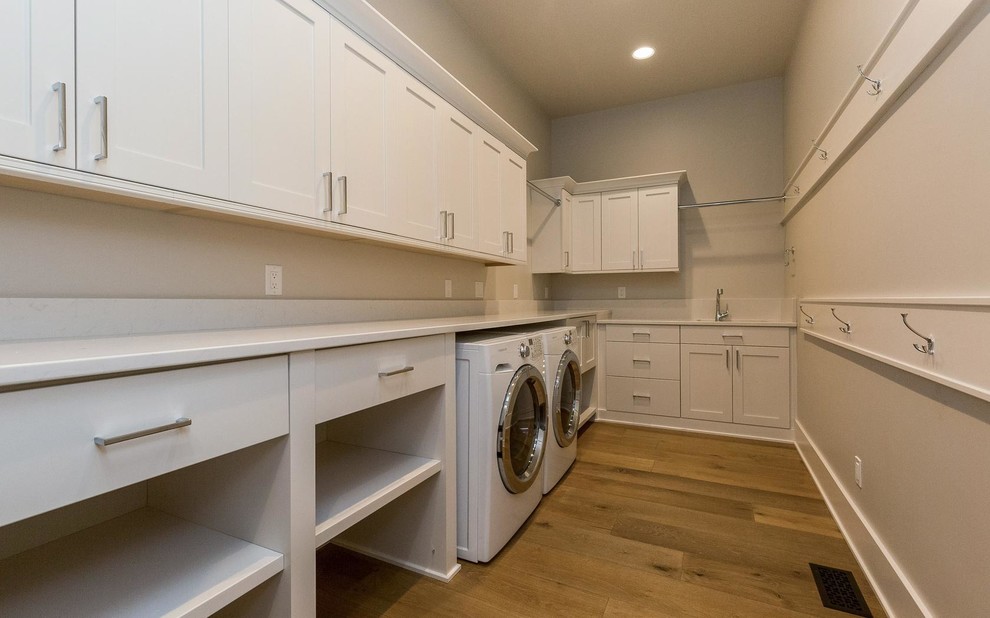 Photo of a mid-sized transitional l-shaped dedicated laundry room in Other with an undermount sink, shaker cabinets, white cabinets, quartz benchtops, grey walls, light hardwood floors and a side-by-side washer and dryer.