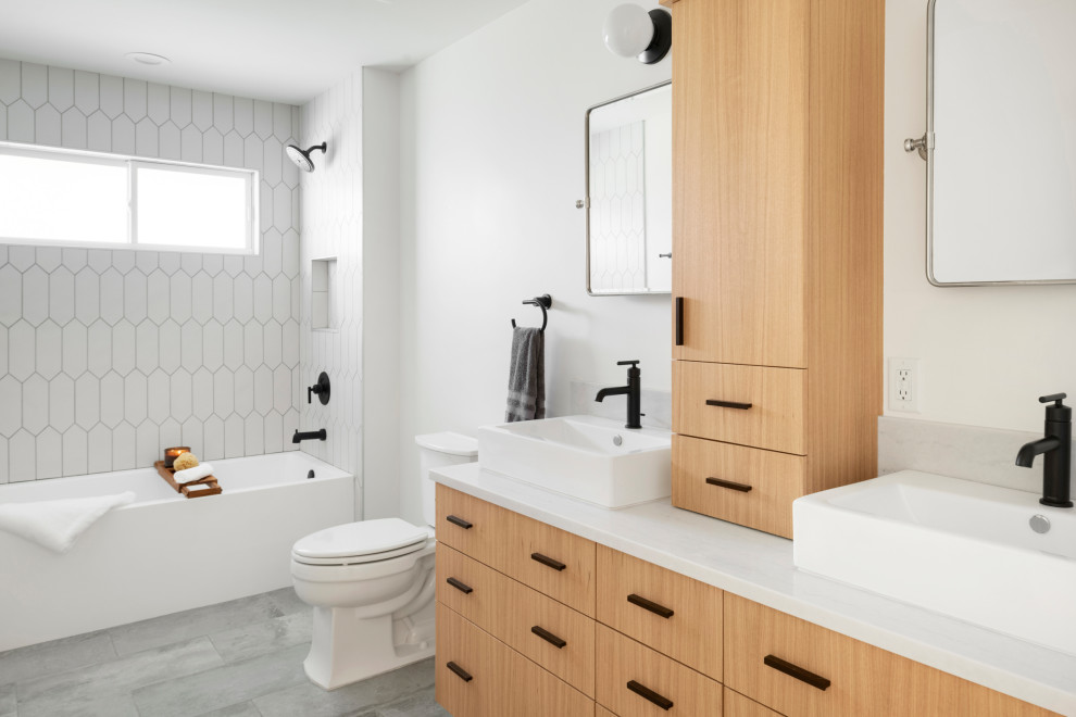 Photo of a mid-sized contemporary 3/4 bathroom in Minneapolis with flat-panel cabinets, light wood cabinets, an alcove tub, a two-piece toilet, white tile, ceramic tile, white walls, ceramic floors, a vessel sink, engineered quartz benchtops, grey floor, white benchtops, a niche, a double vanity, a shower/bathtub combo and an open shower.