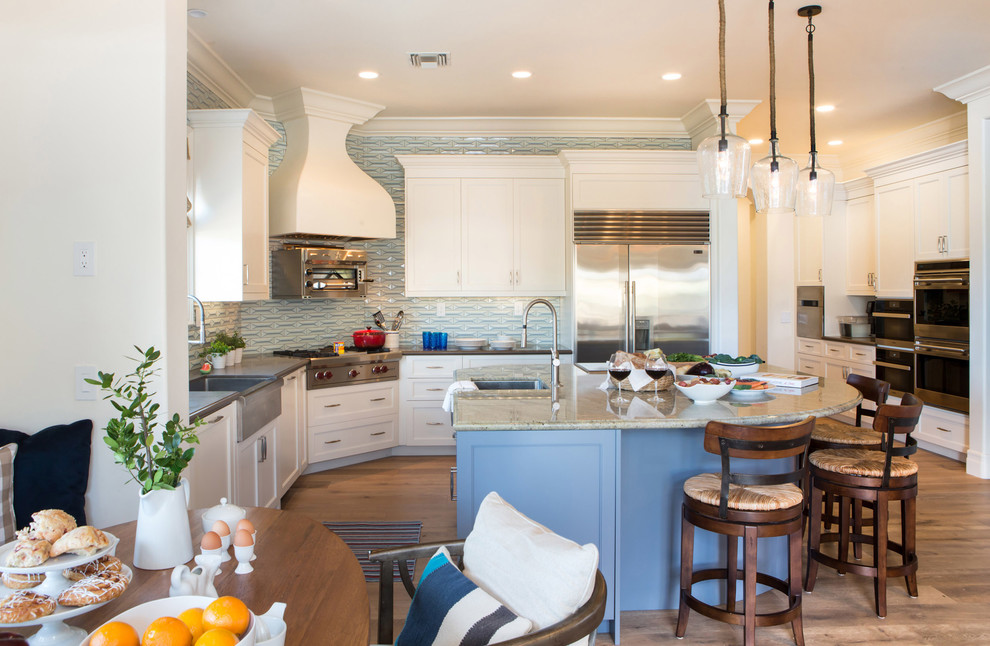 Example of a large transitional u-shaped medium tone wood floor open concept kitchen design in Los Angeles with a farmhouse sink, shaker cabinets, white cabinets, quartz countertops, blue backsplash, ceramic backsplash, stainless steel appliances and an island