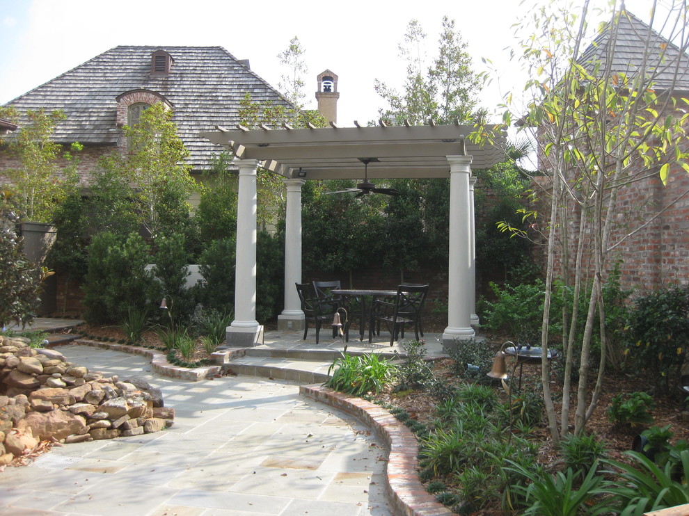 Design ideas for a small country backyard patio in New Orleans with natural stone pavers, a pergola and a water feature.