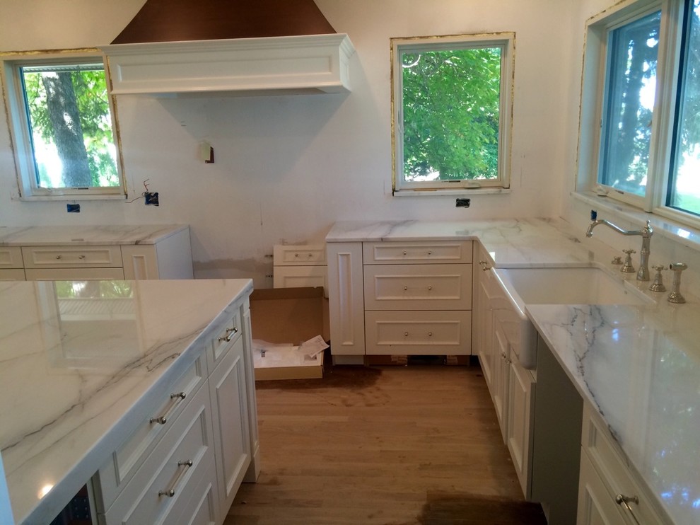 Inspiration for a large country u-shaped eat-in kitchen in Detroit with a farmhouse sink, recessed-panel cabinets, white cabinets, marble benchtops, medium hardwood floors, with island and brown floor.