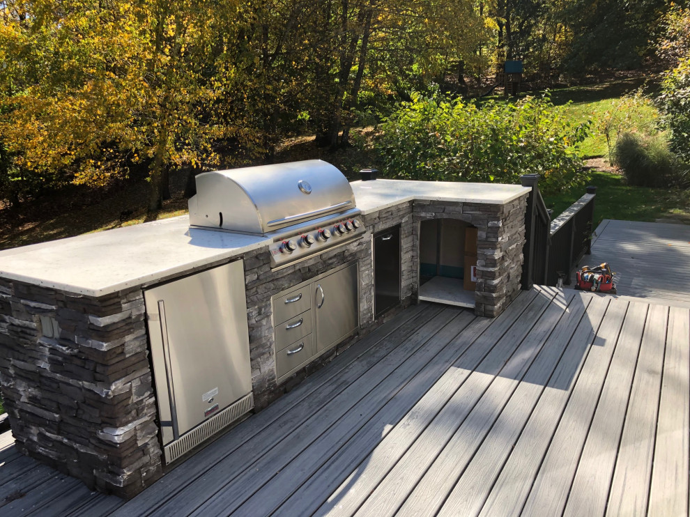 This is an example of a mid-sized modern backyard and ground level deck in New York with an outdoor kitchen, no cover and wood railing.