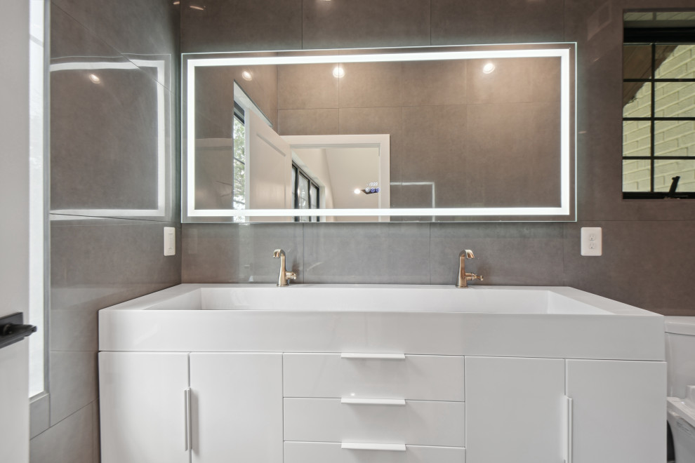 This is an example of a modern master bathroom in DC Metro with flat-panel cabinets, white cabinets, a bidet, gray tile, ceramic tile, grey walls, ceramic floors, a trough sink, solid surface benchtops, grey floor, white benchtops, a double vanity and a floating vanity.