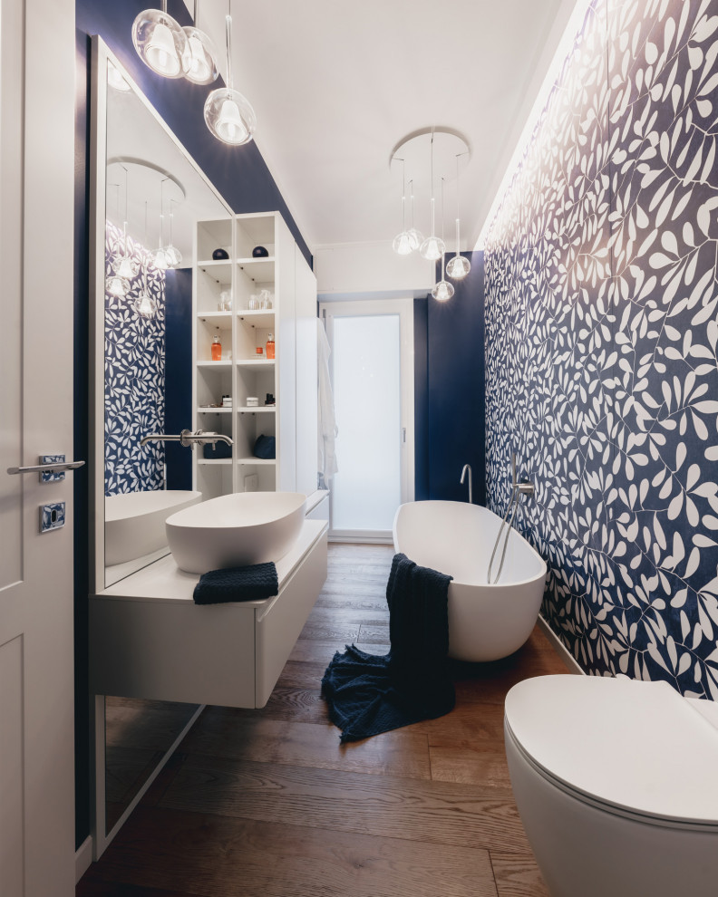 Small bathroom in Milan with flat-panel cabinets, blue cabinets, a freestanding bath, a two-piece toilet, multi-coloured tiles, porcelain tiles, blue walls, dark hardwood flooring, a vessel sink, solid surface worktops, brown floors, white worktops, a single sink and a floating vanity unit.