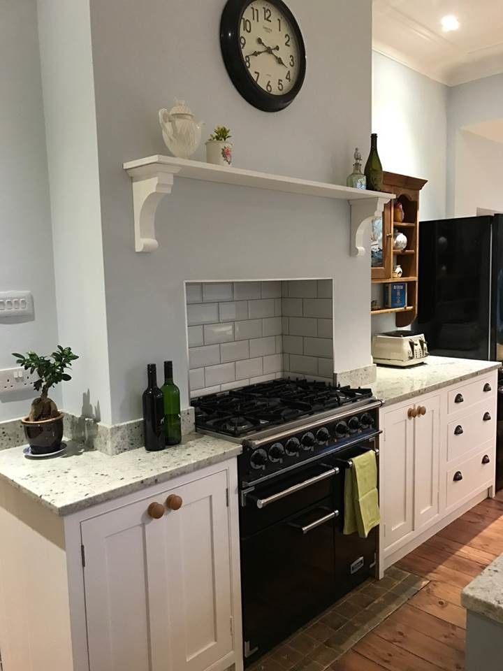 This is an example of a mid-sized country single-wall kitchen in Surrey with a drop-in sink, flat-panel cabinets, with island and white benchtop.