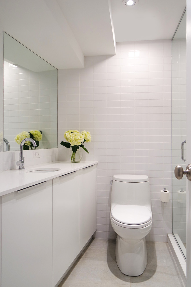 Photo of a contemporary bathroom in New York with flat-panel cabinets, white cabinets, an alcove shower, a one-piece toilet, white tile and an undermount sink.
