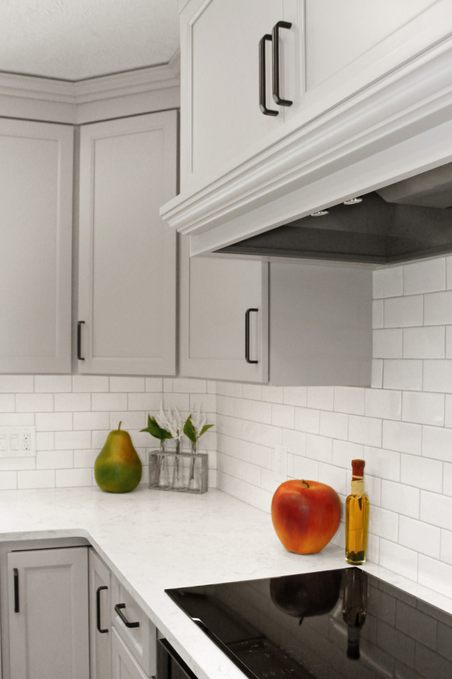Large transitional u-shaped light wood floor and brown floor enclosed kitchen photo in Boston with a double-bowl sink, shaker cabinets, gray cabinets, quartz countertops, white backsplash, porcelain backsplash, black appliances, an island and white countertops