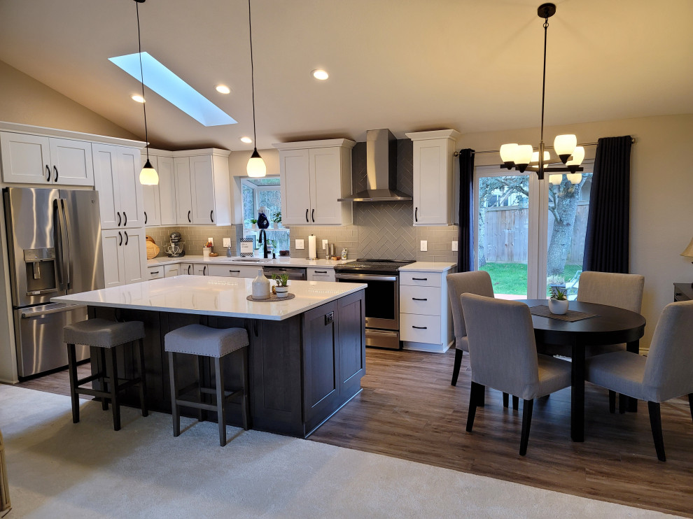 Photo of a l-shaped eat-in kitchen in Seattle with an undermount sink, shaker cabinets, white cabinets, quartz benchtops, grey splashback, glass tile splashback, stainless steel appliances, laminate floors, with island, brown floor, multi-coloured benchtop and vaulted.