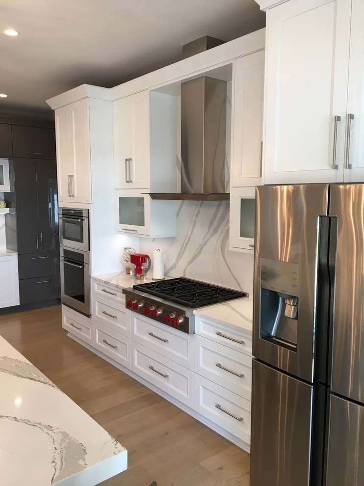 Mid-sized modern single-wall open plan kitchen in New York with an undermount sink, shaker cabinets, white cabinets, stone slab splashback, stainless steel appliances, light hardwood floors and with island.