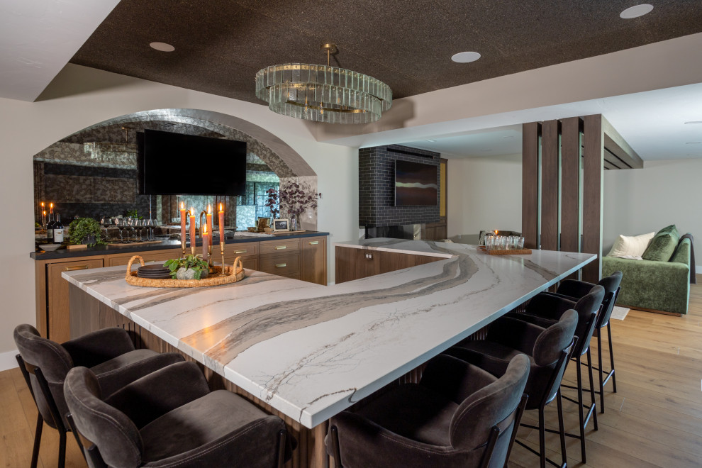 This is an example of a transitional u-shaped seated home bar in Cleveland with an undermount sink, shaker cabinets, medium wood cabinets, marble benchtops, vinyl floors, brown floor and white benchtop.