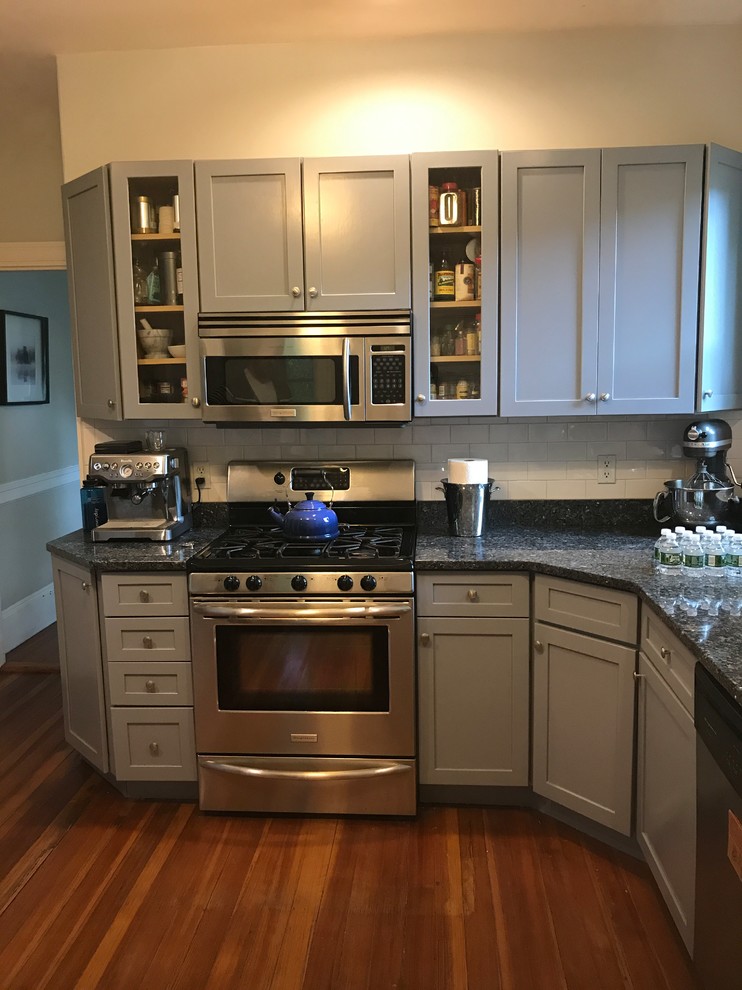 Mid-sized transitional l-shaped medium tone wood floor and brown floor enclosed kitchen photo with an undermount sink, shaker cabinets, gray cabinets, granite countertops, white backsplash, subway tile backsplash, no island and black countertops