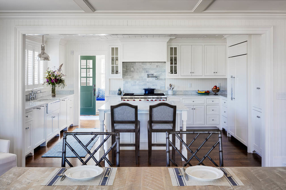 This is an example of a beach style eat-in kitchen in Boston with a farmhouse sink, shaker cabinets, white cabinets, multi-coloured splashback, stainless steel appliances, with island, brown floor and medium hardwood floors.
