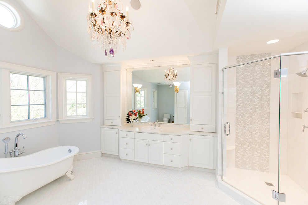 This is an example of an expansive traditional master bathroom in Boston with raised-panel cabinets, white cabinets, a freestanding tub, an alcove shower, ceramic floors, an integrated sink, solid surface benchtops, white floor, a hinged shower door and white benchtops.