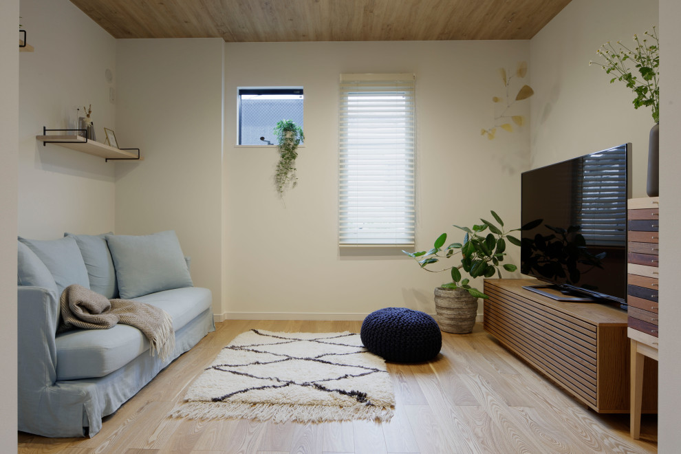 На фото: открытая гостиная комната среднего размера в скандинавском стиле с белыми стенами, светлым паркетным полом, отдельно стоящим телевизором, бежевым полом, потолком с обоями, обоями на стенах и синим диваном без камина с