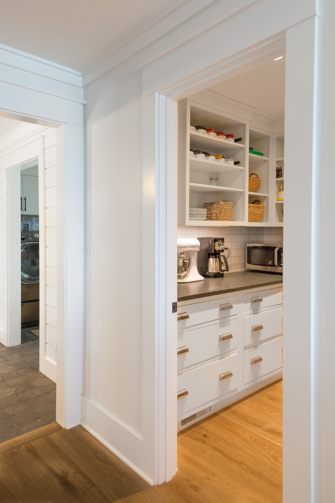 This is an example of a large beach style eat-in kitchen in Boston with an undermount sink, shaker cabinets, white cabinets, granite benchtops, white splashback, subway tile splashback, stainless steel appliances, medium hardwood floors, with island, brown floor and black benchtop.