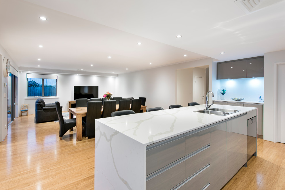 This is an example of a contemporary open plan kitchen in Perth with a double-bowl sink, grey cabinets, quartz benchtops, white splashback, glass sheet splashback, stainless steel appliances, bamboo floors, with island, brown floor and multi-coloured benchtop.