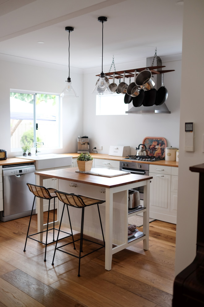 Inspiration for a small transitional l-shaped separate kitchen in Perth with a farmhouse sink, raised-panel cabinets, white cabinets, wood benchtops, stainless steel appliances, medium hardwood floors, with island and brown floor.