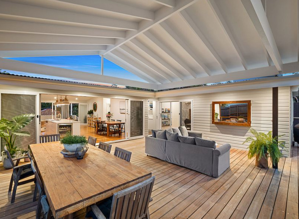 Design ideas for an expansive beach style backyard and ground level deck in Sydney with a roof extension and cable railing.