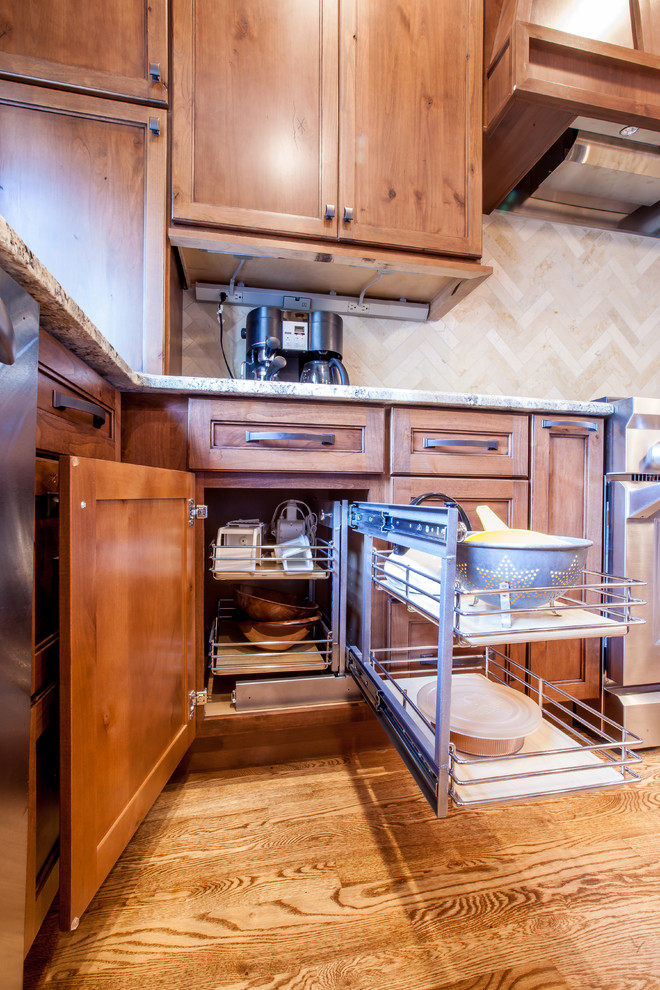 Example of a mid-sized mountain style u-shaped medium tone wood floor and brown floor enclosed kitchen design in Omaha with an undermount sink, shaker cabinets, dark wood cabinets, granite countertops, beige backsplash, travertine backsplash, stainless steel appliances, an island and multicolored countertops