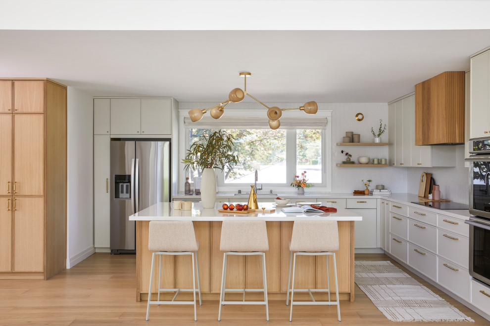 Bild på ett mellanstort minimalistiskt vit vitt kök, med en undermonterad diskho, skåp i shakerstil, skåp i ljust trä, bänkskiva i kvarts, vitt stänkskydd, stänkskydd i keramik, rostfria vitvaror, ljust trägolv, en köksö och brunt golv