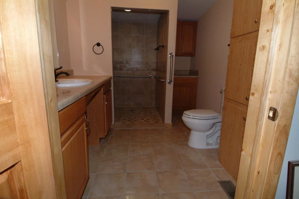 Photo of a mid-sized traditional master bathroom in Other with beaded inset cabinets, medium wood cabinets, an open shower, a two-piece toilet, beige tile, ceramic tile, beige walls, ceramic floors, a drop-in sink, laminate benchtops, beige floor and an open shower.