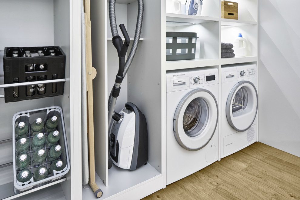 Photo of a large contemporary single-wall laundry room in Barcelona with flat-panel cabinets, white cabinets, light hardwood floors and brown floor.