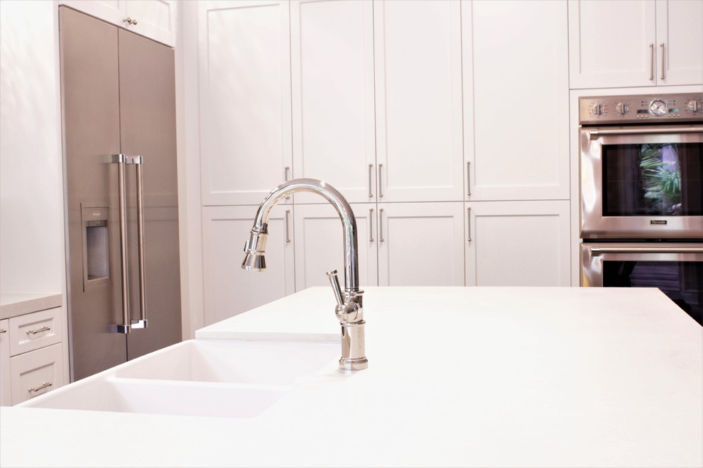 Example of a mid-sized transitional l-shaped light wood floor and gray floor eat-in kitchen design in Houston with a farmhouse sink, recessed-panel cabinets, white cabinets, quartz countertops, white backsplash, ceramic backsplash, stainless steel appliances, an island and white countertops