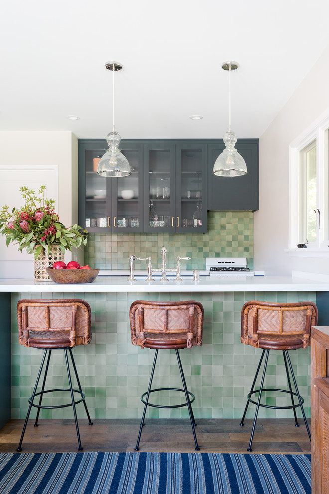 This is an example of a small beach style galley open plan kitchen in Los Angeles with recessed-panel cabinets, grey cabinets, green splashback, mosaic tile splashback, medium hardwood floors, a peninsula, brown floor, white benchtop, a farmhouse sink, quartzite benchtops and panelled appliances.