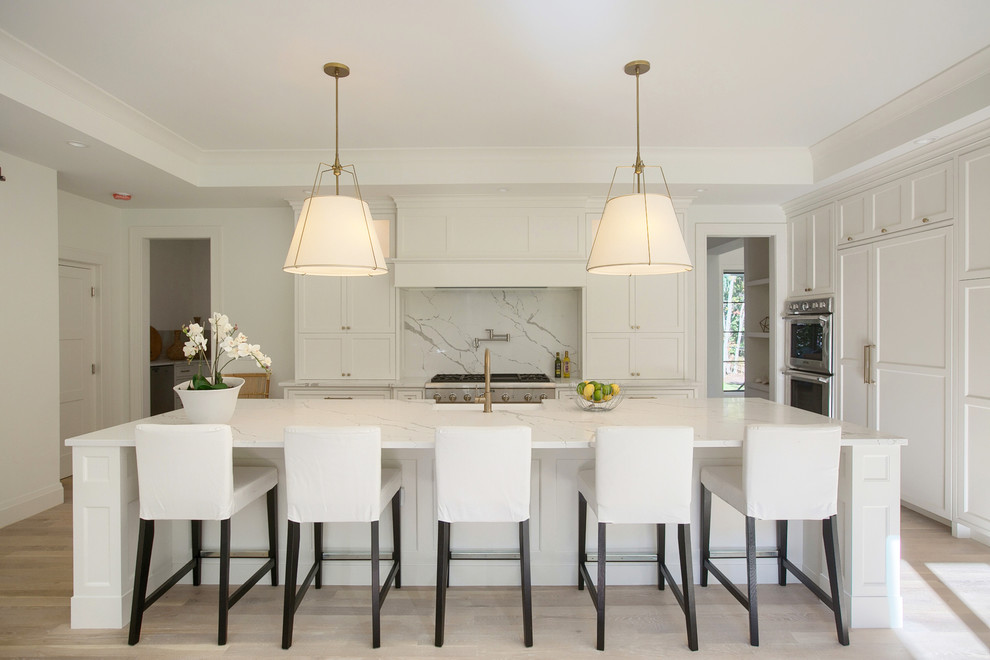 Photo of a transitional kitchen in Boston with shaker cabinets, white cabinets, white splashback, panelled appliances, light hardwood floors, with island and beige floor.