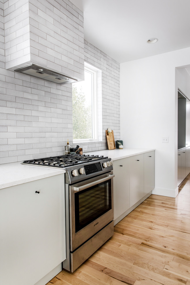 Photo of a large scandinavian single-wall eat-in kitchen in Grand Rapids with an undermount sink, flat-panel cabinets, grey cabinets, quartzite benchtops, grey splashback, brick splashback, stainless steel appliances, light hardwood floors, with island, beige floor and white benchtop.