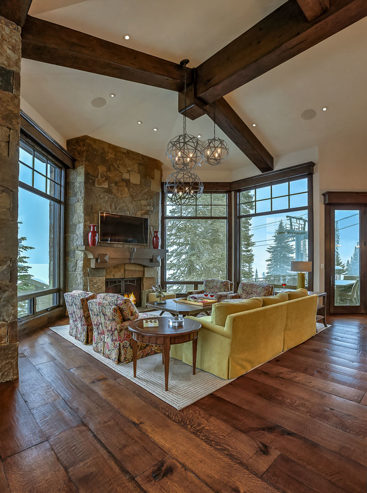 Inspiration for an expansive country open concept living room in Salt Lake City with beige walls, medium hardwood floors, a standard fireplace, a stone fireplace surround and a wall-mounted tv.