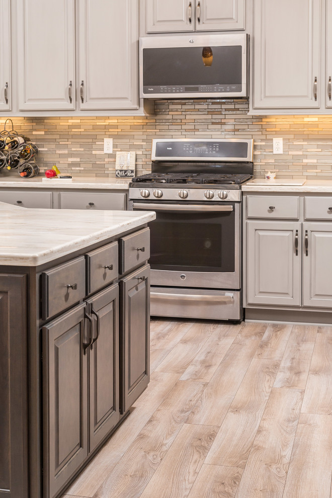 Mid-sized transitional l-shaped open concept kitchen photo with an undermount sink, raised-panel cabinets, gray cabinets, solid surface countertops, metallic backsplash, mosaic tile backsplash, stainless steel appliances and an island