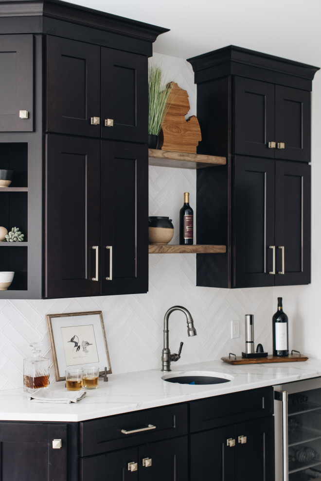 This is an example of a large modern single-wall wet bar in Grand Rapids with an undermount sink, shaker cabinets, black cabinets, quartz benchtops, white splashback, ceramic splashback, porcelain floors, grey floor and white benchtop.