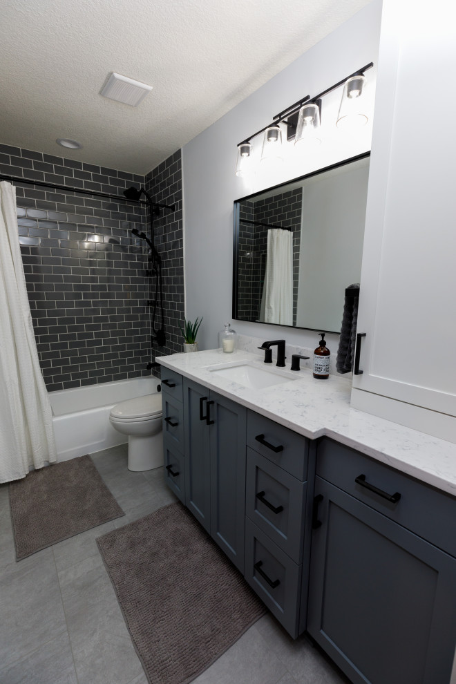 This is an example of a mid-sized transitional bathroom in Minneapolis with recessed-panel cabinets, grey cabinets, an alcove tub, a shower/bathtub combo, a two-piece toilet, gray tile, subway tile, white walls, ceramic floors, an undermount sink, engineered quartz benchtops, grey floor, a shower curtain, white benchtops, a single vanity and a built-in vanity.