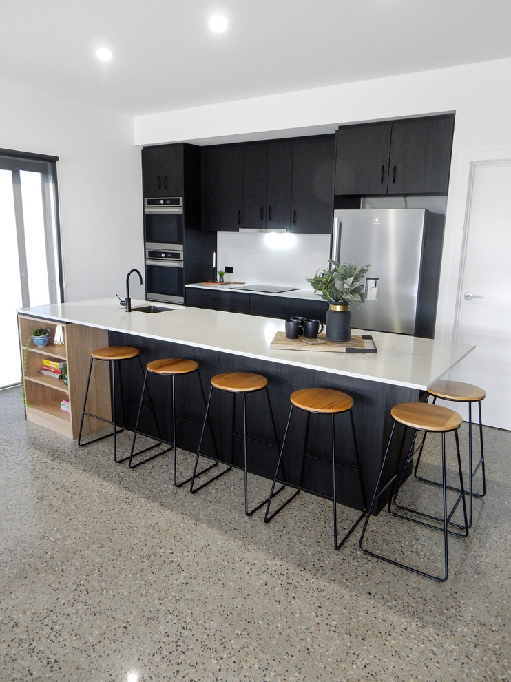 This is an example of a large transitional galley open plan kitchen in Other with an undermount sink, recessed-panel cabinets, black cabinets, quartz benchtops, white splashback, stone slab splashback, stainless steel appliances, concrete floors, with island, multi-coloured floor and white benchtop.