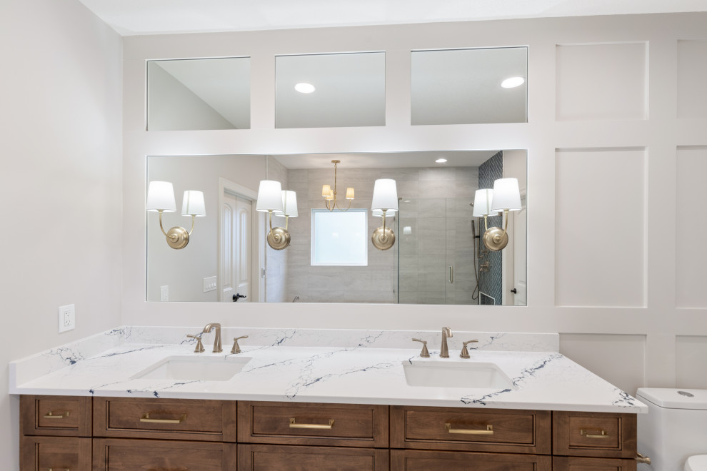 Photo of a medium sized classic ensuite bathroom in Kansas City with flat-panel cabinets, medium wood cabinets, a built-in bath, a corner shower, a one-piece toilet, grey tiles, cement flooring, a submerged sink, engineered stone worktops, grey floors, a hinged door, white worktops, a wall niche, double sinks, a built in vanity unit and wainscoting.