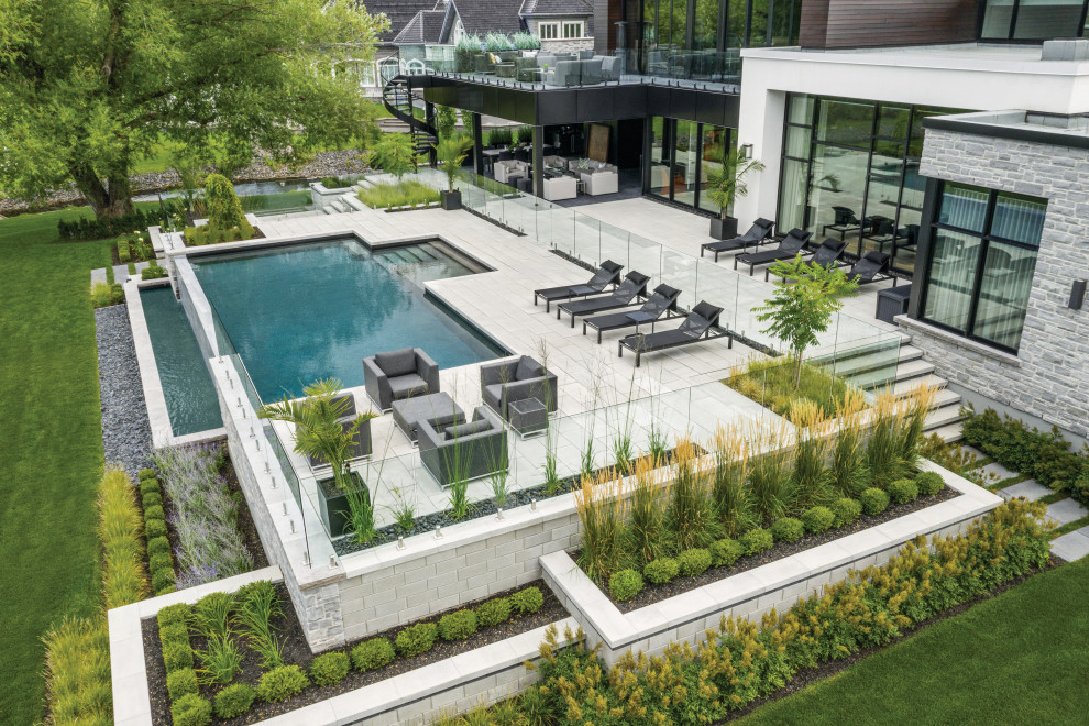 Modelo de piscina alargada minimalista grande rectangular en patio trasero con paisajismo de piscina y losas de hormigón
