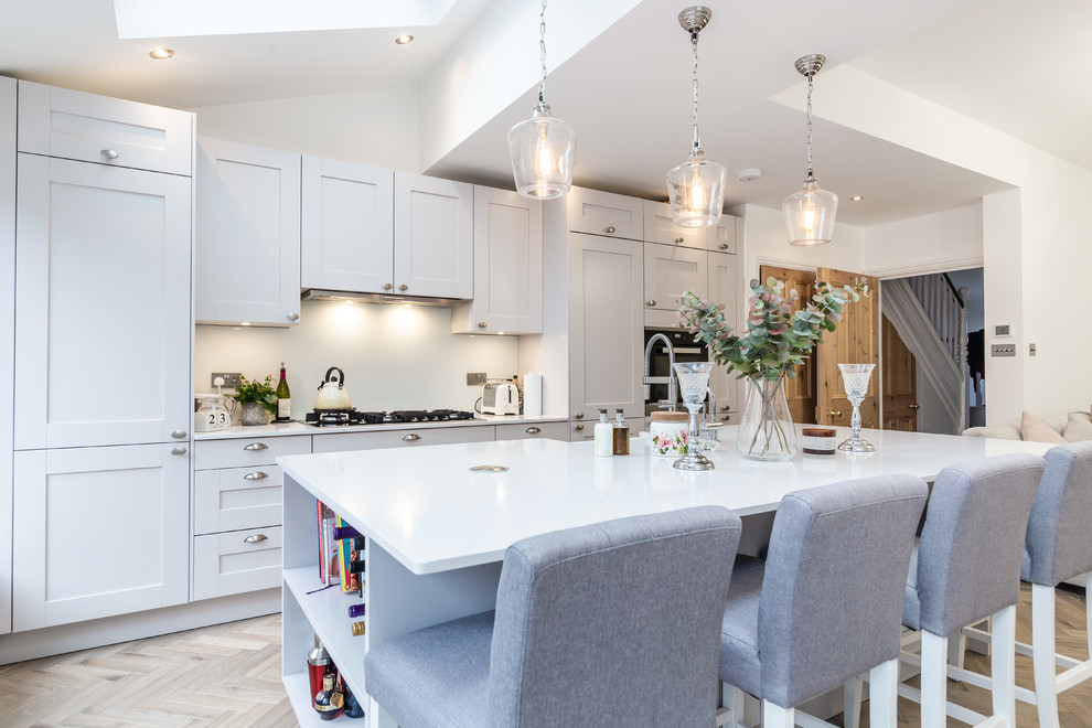 Photo of a large modern kitchen in London with a farmhouse sink, shaker cabinets, quartzite benchtops, white splashback, glass sheet splashback and with island.