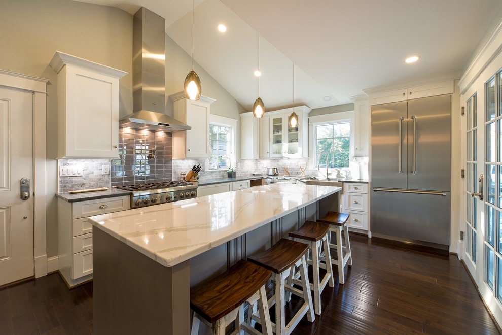 Inspiration for a mid-sized beach style l-shaped eat-in kitchen in DC Metro with a farmhouse sink, flat-panel cabinets, white cabinets, quartz benchtops, grey splashback, porcelain splashback, stainless steel appliances, dark hardwood floors and with island.