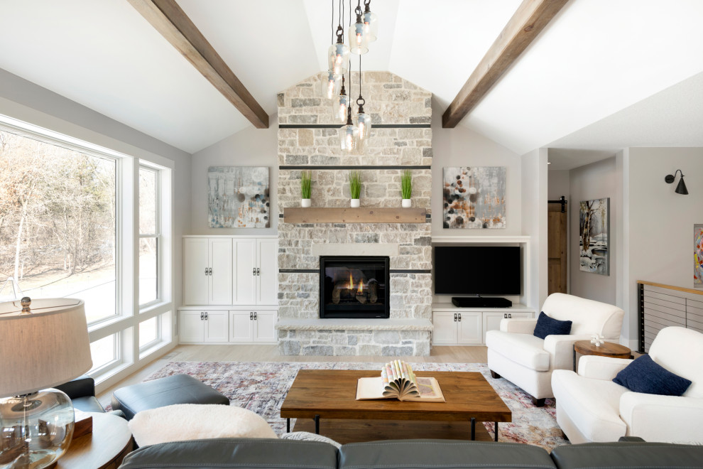 Inspiration for a transitional loft-style living room in Minneapolis with grey walls, light hardwood floors, a standard fireplace, a stone fireplace surround, beige floor, exposed beam and vaulted.