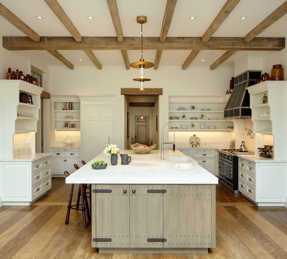 Design ideas for a country kitchen in Boston with a farmhouse sink, open cabinets, white cabinets, white splashback, black appliances, light hardwood floors, with island and white benchtop.