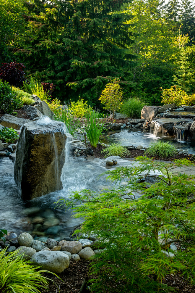 Expansive arts and crafts backyard garden in Seattle with with waterfall and natural stone pavers.