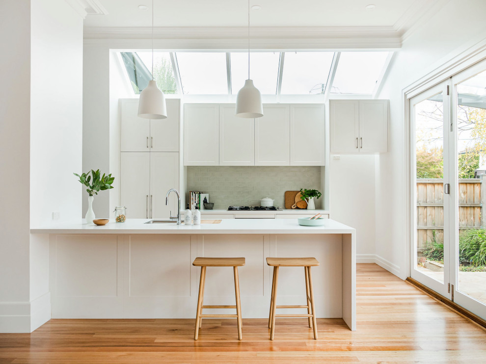 Photo of a mid-sized contemporary galley eat-in kitchen in Melbourne with a drop-in sink, shaker cabinets, white cabinets, quartzite benchtops, ceramic splashback, stainless steel appliances, light hardwood floors, with island and white benchtop.